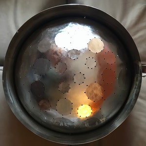 May include: A silver colander with a round, bowl-shaped design and a large number of small holes. The colander is made of metal and has a shiny, reflective surface.