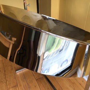 May include: A shiny silver steel drum with a stand. The drum is round and has a slight curve to it. The stand is made of metal and has a black finish.