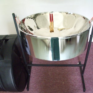 May include: A silver steel pan drum with a black stand and a black padded carrying case. Two red drumsticks are resting on the drum.