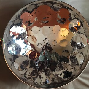 May include: A silver steel pan with a circular shape and multiple round indentations. The pan has two green and orange cords attached to the sides.