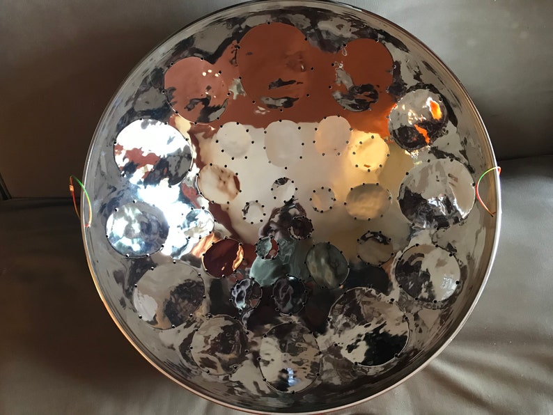 May include: A silver steel pan with a circular shape and multiple round indentations. The pan has two green and orange cords attached to the sides.