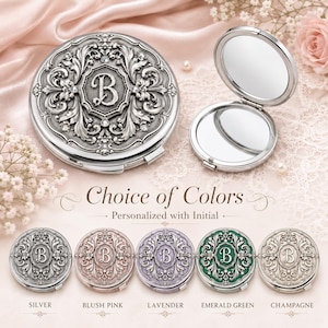 May include: A round, silver-toned compact mirror featuring an ornate, embossed floral design with a central letter B and small embedded crystals. The set includes an open mirror and five color variations labeled Silver, Blush Pink, Lavender, Emerald Green, and Champagne, with the text Choice of Colors and Personalized with Initial.