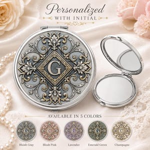May include: A round silver-toned compact mirror featuring an ornate embossed floral pattern and a central diamond-shaped plaque with the letter G. The set includes one closed mirror and one open mirror, with text reading Personalized With Initial.