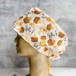 May include: A white scrub hat with a yellow button and a repeating pattern of brown and yellow ice cream cones with the text "Whip It" on each cone.