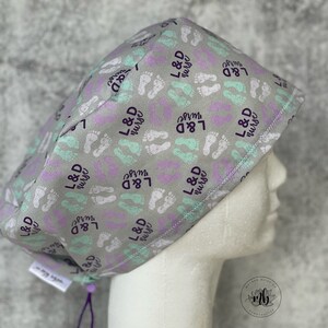 May include: Gray scrub hat with a purple and teal footprint pattern and the text "L&D nurse" repeated throughout.