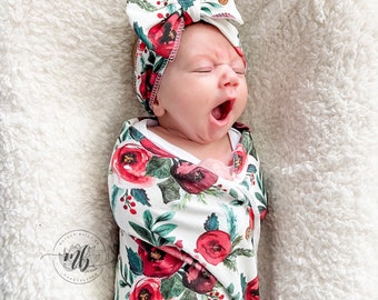 Könnte beinhalten: Ein Baby, das in ein weißes und rotes Blumenmuster-Swaddle gewickelt ist, mit einem passenden roten und weißen Blumenmuster-Stirnband. Das Baby gähnt und trägt ein weißes Stirnband mit einer großen Schleife.
