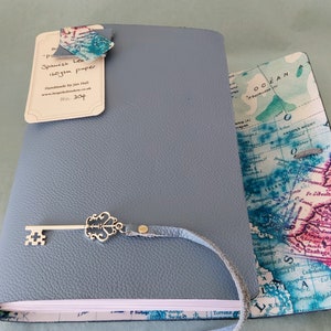 May include: A blue leather journal with a key charm and a map design on the cover. The journal is handmade and has a label that says "Spanish Leather 120gsm paper Handmade by Jan Hall No. 304".