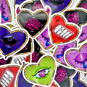 May include: A collection of heart-shaped stickers with various designs. The stickers feature different colors, patterns, and details, including eyes, teeth, and dripping paint. The stickers are perfect for adding a unique touch to journals, laptops, water bottles, and other surfaces.