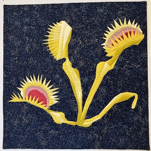 May include: A quilted wall hanging featuring a stylized depiction of Venus flytraps. The artwork showcases yellow and cream-colored plant forms against a dark blue background with a speckled pattern. The flytraps have red and pink interiors.