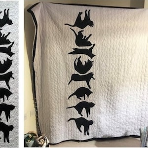 May include: A white quilt featuring a black silhouette of a cat repeated down the centre. The cat is in various poses, creating a playful and whimsical design.