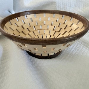 May include: A handcrafted wooden bowl with a woven design. The bowl features a light-colored wood interior and a dark brown rim and base. The woven pattern creates an open, airy aesthetic, perfect for displaying fruit or decorative items.