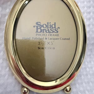 Può includere: Una cornice portafoto ovale in ottone massiccio con finitura lucida e due piccoli piedini sferici alla base. L'inserto riporta: Solid Brass PHOTO FRAME Hand Polished & Lacquer Coated 3 1/2 inches x 5 inches, 9 cm x 13 cm.