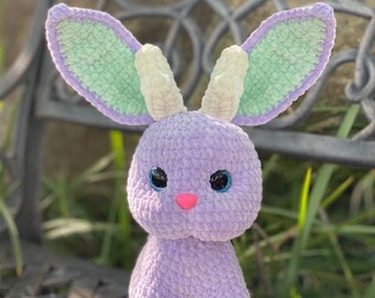 May include: A crocheted purple bunny with green and white ears. The bunny is sitting on a woven chair.