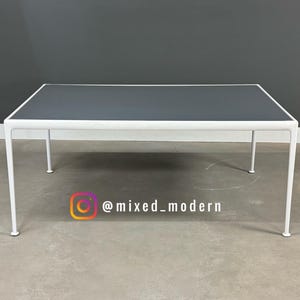May include: A rectangular coffee table with a dark gray top and white legs. The table is a modern design with a minimalist aesthetic. The table is approximately 48 inches long, 24 inches wide, and 16 inches high.