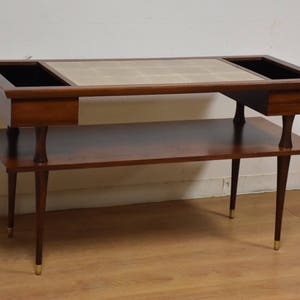 May include: A mid-century modern coffee table with a tiled top and two built-in planters. The table has a lower shelf and is made of dark wood with brass accents.