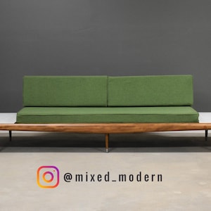 May include: A mid-century modern sofa with a green cushion and backrest. The sofa has a wooden frame with attached white side tables. The design is minimalist and features clean lines. The Instagram handle @mixed_modern is visible.