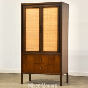 May include: A mid-century modern cabinet with two doors and two drawers. The doors are made of wood and have a woven cane panel. The cabinet is finished in a rich brown color.