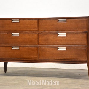 May include: A six-drawer dresser made of dark wood with silver drawer pulls. The dresser has a simple, mid-century modern design.