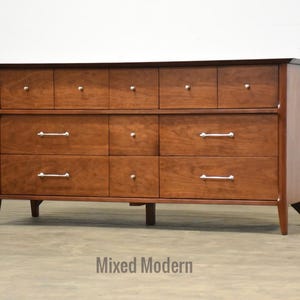 May include: A large, wooden dresser with nine drawers and silver hardware. The dresser has a dark wood finish and a simple, modern design.