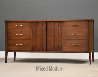 May include: A mid-century modern wooden dresser with six drawers and two cabinet doors. The dresser is a warm brown color with gold-toned hardware and a curved top. The text "Mixed Modern" is at the bottom.
