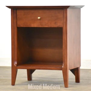 May include: A wooden nightstand with a single drawer and a shelf. The nightstand is a rich brown color and has a simple, modern design.