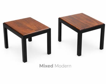 May include: Two square side tables with dark wood tops and black metal frames. The tables have a minimalist design, with clean lines and a modern aesthetic. The tables are approximately 20 inches wide and 20 inches long.