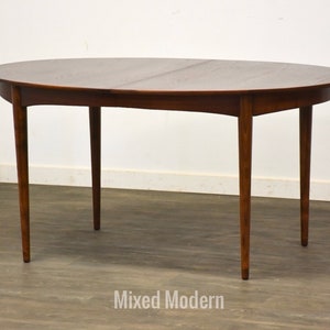 May include: A mid-century modern oval dining table with a rich brown finish. The table features a smooth tabletop and four slender, tapered legs. The table is approximately 60 inches long and 40 inches wide.