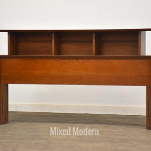 May include: A wooden headboard with a built-in shelf above the headboard. The headboard is a rich brown color and has a simple, modern design.