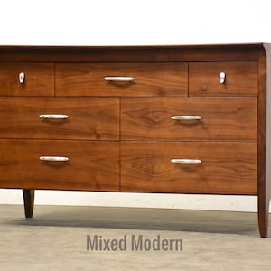May include: A six-drawer dresser with a walnut wood finish and silver drawer pulls. The dresser has a curved top and tapered legs.