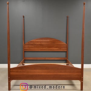 May include: A wooden four-poster bed frame with a headboard and footboard. The frame is made of a reddish-brown wood and features four tall posts with finials. The bed frame is empty and ready for a mattress. The Instagram handle @mixed_modern is visible.
