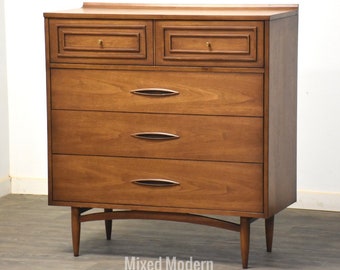 May include: A mid-century modern dresser with five drawers and tapered legs. The dresser is made of wood and has a warm brown finish.