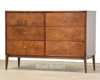 May include: A six-drawer dresser with a light wood finish and brass hardware. The dresser has a simple, mid-century modern design with tapered legs.