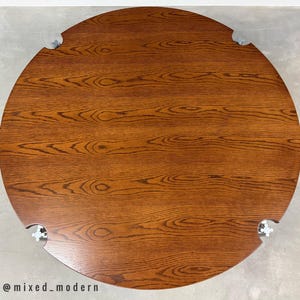 May include: Overhead view of a round wooden table with a rich, warm brown finish. The table's surface showcases a prominent wood grain pattern. The table has a unique design with cut-out sections and metal hardware. A modern furniture piece.