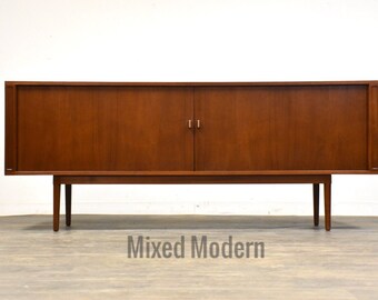 May include: A long, rectangular, mid-century modern sideboard with two sliding doors and a wood grain finish. The sideboard is supported by four slender legs.