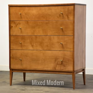 May include: A light wood dresser with four drawers and brass hardware. The dresser has a simple, mid-century modern design and sits on four tapered legs.