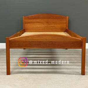 May include: A wooden bed frame with a headboard and footboard. The bed frame is made of a light brown wood and has a slatted base. The headboard has a curved top. The Instagram handle @mixed_modern is visible.