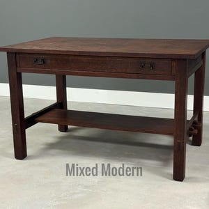 May include: A dark brown wooden desk with a rectangular top, two drawers, and a lower shelf. The desk has a classic design with square legs and decorative hardware. The text "Mixed Modern" is visible at the bottom.