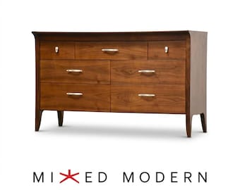 May include: A brown wooden dresser featuring seven drawers with silver-toned metal handles. The top row has three smaller drawers, while the bottom two rows each contain two larger drawers. The text MIXED MODERN is displayed below.