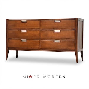 May include: A brown wooden dresser featuring six drawers arranged in two columns of three. Each drawer is equipped with a rectangular silver metal pull handle. The piece stands on four tapered legs and includes the text MIXED MODERN below it.