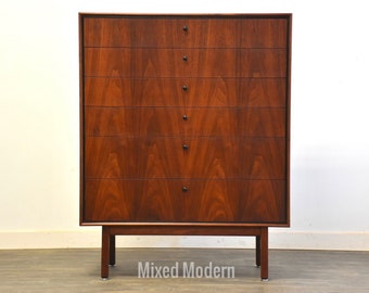 May include: A six-drawer dresser made of dark wood with black hardware. The dresser has a simple design with straight lines and a slightly tapered base.
