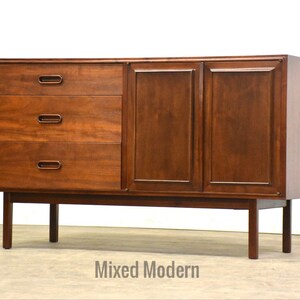 May include: A mid-century modern wooden dresser with three drawers and two cabinet doors. The dresser is made of dark wood and has a simple design.