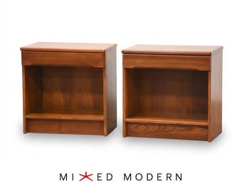 May include: A pair of matching wooden nightstands featuring a warm brown finish, each with a single top drawer and an open storage shelf below. The text MIXED MODERN is printed in black below the furniture with a red star symbol in the center.