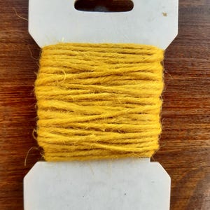 May include: A spool of yellow twine wrapped in a white cardboard holder with a hanging hole.