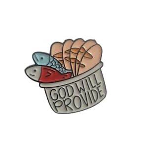 May include: A silver-colored enamel pin featuring a stylized illustration of two fish and several loaves of bread in a container. The text "GOD WILL PROVIDE" is printed on the container in black letters.