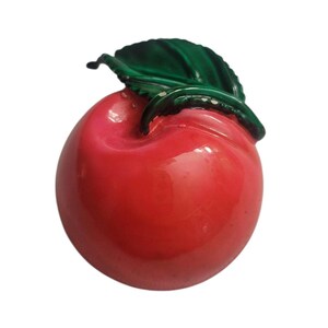May include: A glossy, red apple figurine with a green leaf. The apple has a smooth, reflective surface and a slight indentation on one side. The green leaf is detailed with visible veins and adds a natural touch to the decorative piece.