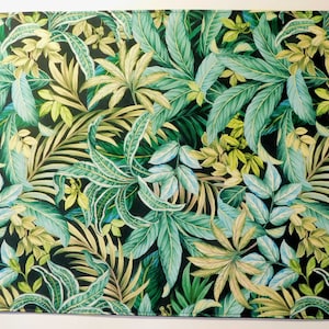 Puede incluir: Un mantel individual de tela con estampado de hojas tropicales verdes y amarillas. El mantel individual tiene un fondo verde oscuro con una variedad de hojas verdes y amarillas.