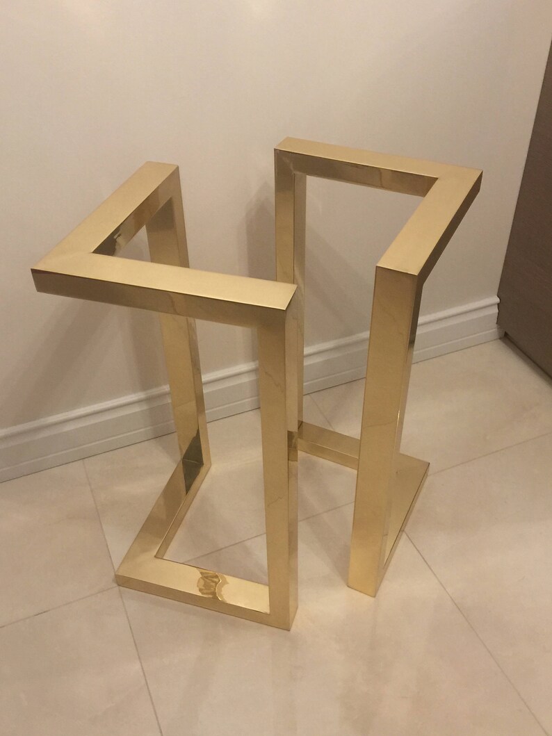 May include: A gold metal stand with a geometric design. The stand is made of square tubing and has a rectangular base.
