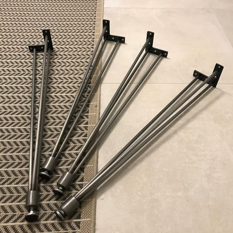 May include: Four black metal hairpin legs for furniture. Each leg has three prongs and a flat base.