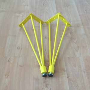 May include: Two yellow metal table legs with a triangular base and five prongs each. The legs have black rubber feet.
