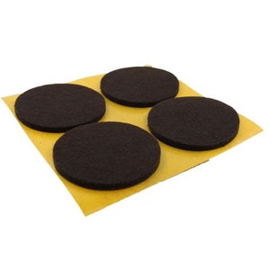 May include: Four brown felt furniture pads with adhesive backing on a yellow sheet. The pads are circular and designed to protect floors from scratches.